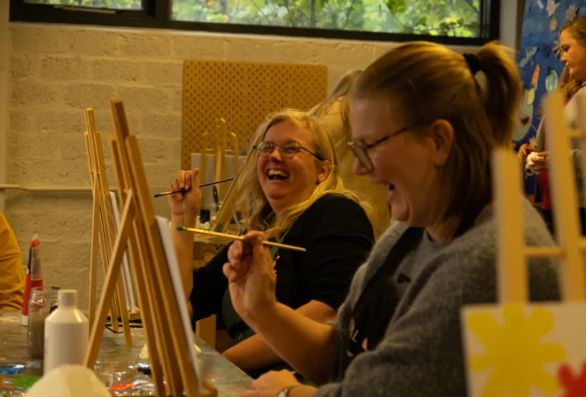Twee vrouwen zitten naast elkaar en lachen tijdens het schilderen