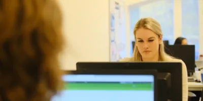 In een kantoorruimte zit een vrouw voor haar computer te werken. Ze kijkt naar het scherm.