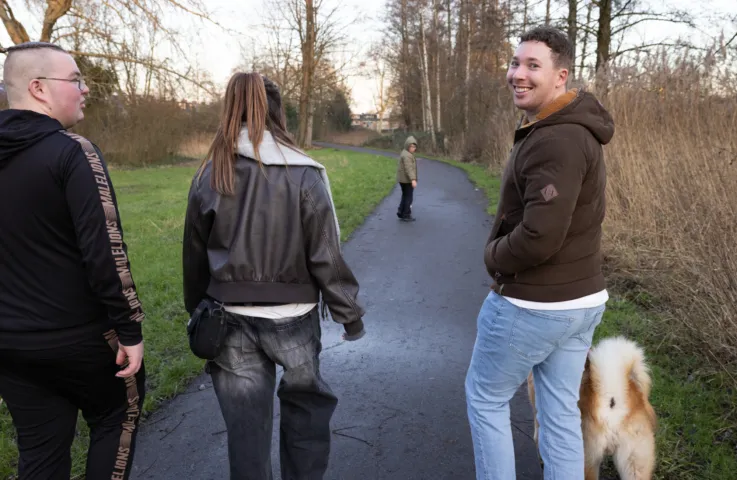 Drie mensen en in de verte een kind zijn aan het wandelen in een park met de hond